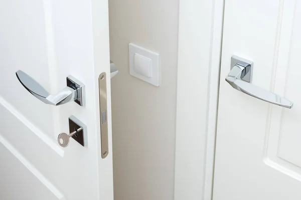 Modern chrome door handle and lock with key. White interior door closeup