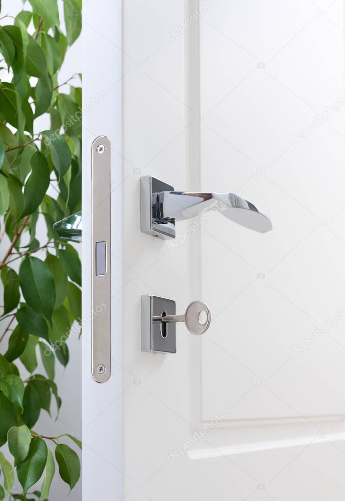 Closeup of door fittings. A white door with modern chrome handles, door lock with key