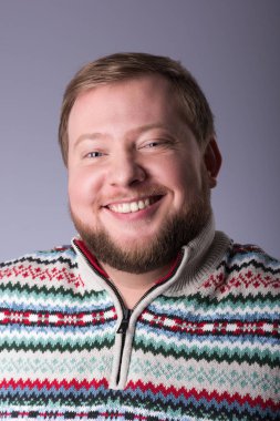 Bir sakallı bir genç adam kazak giyiyor. Geniş bir gülümseme