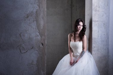 Beyaz bir gelinlikle beton duvara yanında genç bir kadın. Yatay moda fotoğrafçılığı