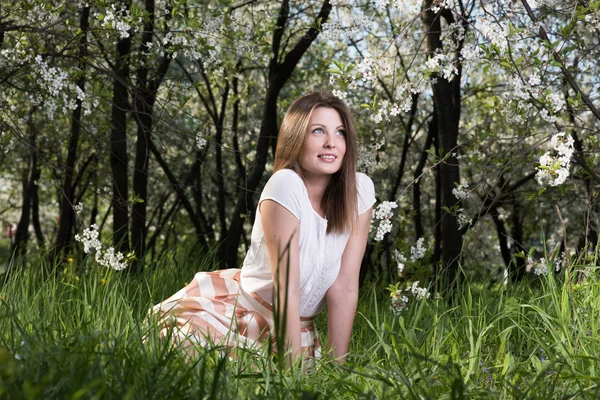 Jovem mulher sentada na grama no exuberante jardim. Retrato de primavera na natureza — Fotografia de Stock