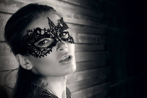 Black and white closeup portrait of a beautiful young woman in elegant masquerade mask