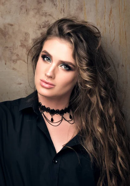 Vertical closeup portrait of young beautiful woman in black shirt posing in front of a metal wall — Stock Photo, Image