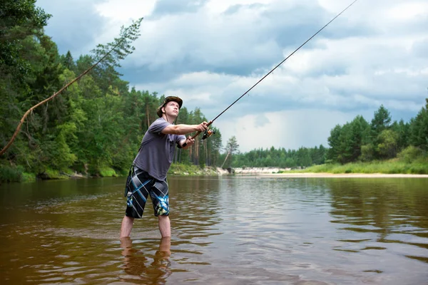 Pesca antes de la tormenta. Un joven atrapa un pez al girar, de pie en el río —  Fotos de Stock