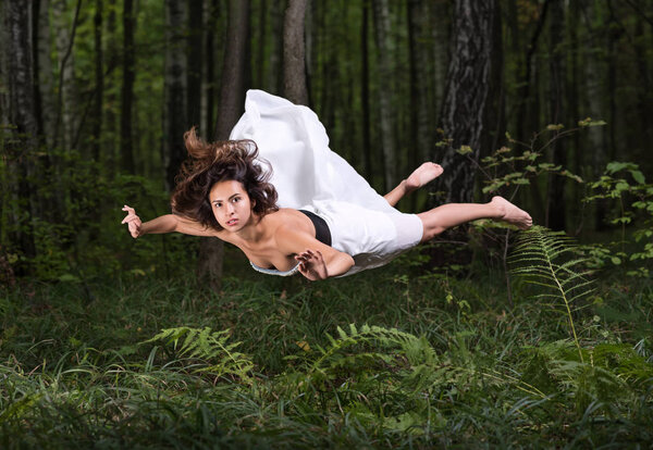 Нулевая гравитация. Молодая красивая женщина летит во сне в летнем лесу

