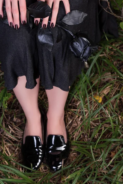 Женские ноги в черных кожаных ботинках на траве. Черная юбка и роза — стоковое фото