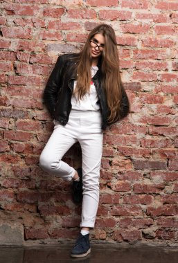 Bir tuğla duvara poz genç çekici kadın. Şık görünümü, siyah deri ceket