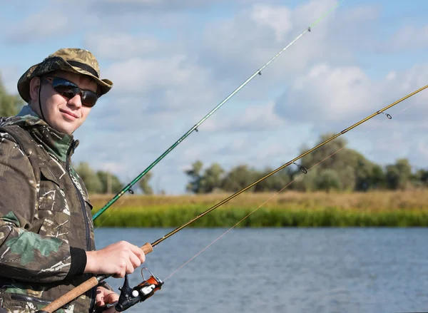 Un pescador con una caña giratoria para pescar. Gafas de sol y ropa de pesca — Foto de Stock