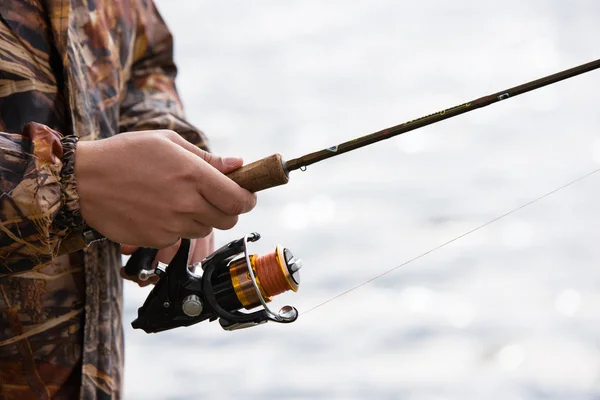 Un pescador atrapa un pez. Manos de un pescador con una caña de hilar en primer plano — Foto de Stock