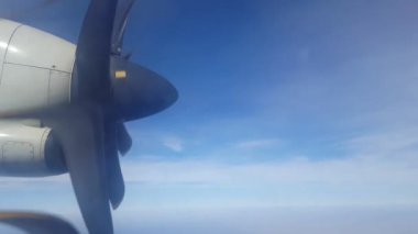 Bulutların üzerindeki mavi gökyüzüne karşı uçağın penceresinden çıkan ATR pervanesi