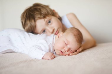 Beyaz pijama karnına büyük kardeşi sarılarak uyuyan bebek