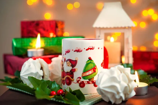 Kerst feestelijke samenstelling - een mok met Santa Klais, gebakjes, kaarsen, takken van holly, bessen en vakken giften op de achtergrond de brandende vuren — Stockfoto