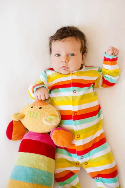 Мила дитина зі смугастою кольоровою піжамою та котячою іграшкою, що лежить на ліжку — стокове фото