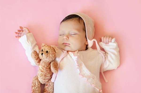 Menina em chapéu branco e pijama rosa abraçando ursinho de pelúcia dorme em sua corrente sanguínea em um cobertor — Fotografia de Stock