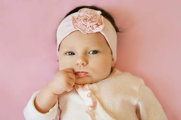 Menina séria olhando para a câmera deitada no fundo rosa. Retrato de um pouco bonito — Fotografia de Stock