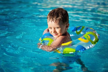 Mutlu küçük beyaz çocuk öğrenme Yüzme Havuzu, diş gülen koruyucuda ile bir hayat halka içinde yüzme keyfini .