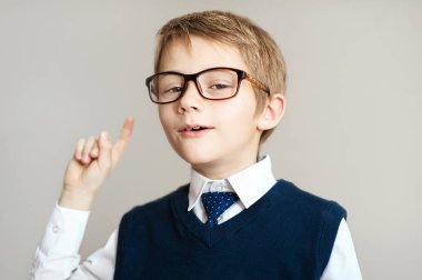 Gri arka plan üzerinde parmak gösterilmesini büyük gözlüklü genç çocuk gülümseyen