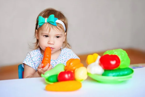 La niña está jugando en la mesa con verduras. Niño vegetariano. Concepto de alimentación saludable — Foto de Stock