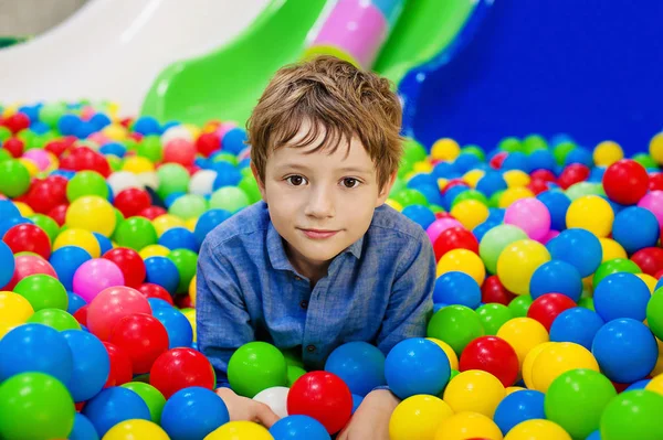 Menino se divertindo brincando com bolas plásticas coloridas . — Fotografia de Stock