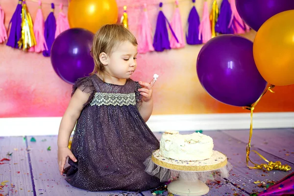 Two year old baby eating cake. Holiday birthday. Decor garlands and balloons