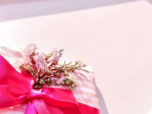 Pembe kurdeleli bir hediye ve pembe arka planda bir buket çiçek. Doğum günü kutlaması. Dekorasyon hediyesi. Boşluğu kopyala.