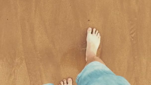 Вид сверху на мужские ноги в свернутых джинсах и босых ногах, идущих рядом с океаном — стоковое видео