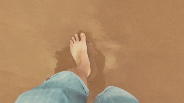 Point of View kijkend naar beneden op mannelijke benen met opgerolde jeans en blote voeten wandelen in de buurt van de Oceaan — Stockvideo