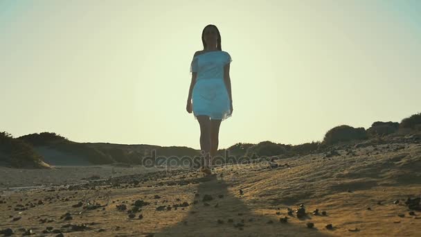 Flicka i vit klänning promenader från solnedgång till kameran. Öknen. Slow motion. — Stockvideo