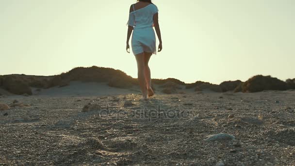 Menina de vestido branco andando até o pôr do sol da câmera. Deserto. Movimento lento . — Vídeo de Stock