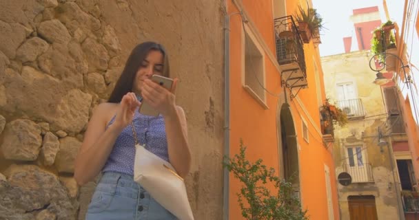 Jonge vrouw lachend verblijf in stad in de ochtend en het gebruik van de smartphone. Meisje surfen op het Internet, texting met iemand. — Stockvideo