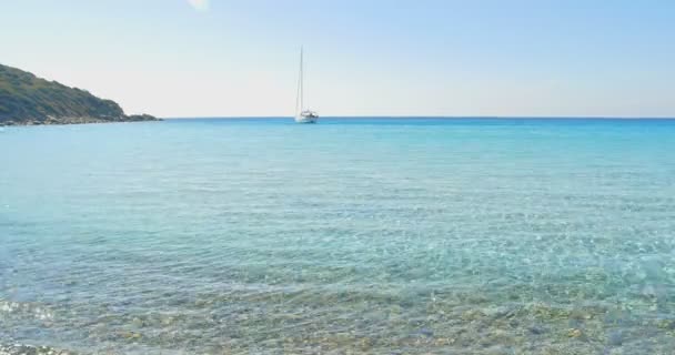 Onde che atterrano su spiaggia di pietra. Yacht all'orizzonte. Acqua cristallina blu . — Video Stock