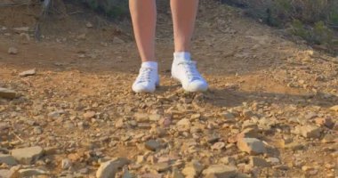 Güzel kadın bacaklar beyaz spor ayakkabı, taşlı zemin boyunca gidiyor. Çölde yürürken.