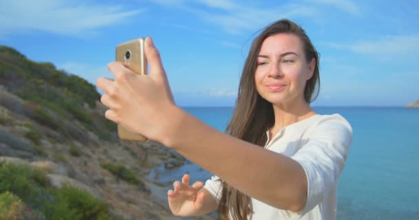 Fiatal, csinos nő selfie fénykép használ a smartphone, tengerre néző csinál. Női állt közel a tenger, naplemente alatt. Tiszta kék víz. — Stock videók