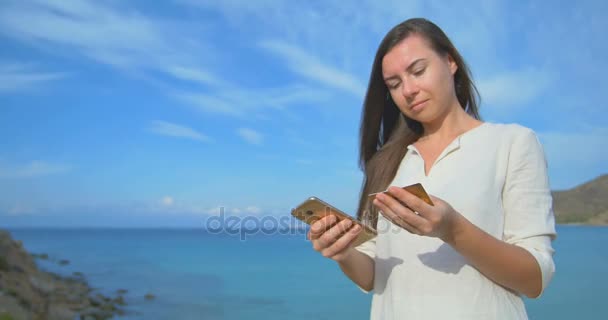 Vrouw met creditcard op vakantie winkelen online met mobiele telefoon tegen de achtergrond van de helderblauwe zee — Stockvideo