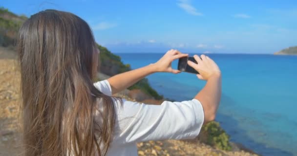 Aantrekkelijke vrouwen maken van foto's van zee met smartphone. Heuvels en helder blauw water. — Stockvideo