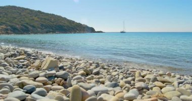 Taş kumsalda açılış dalgalar. Ufukta yat. Açık mavi su.