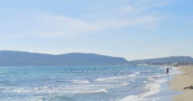 Dalgalar kumsalda iniş. Kadın yürüyor. Açık mavi su