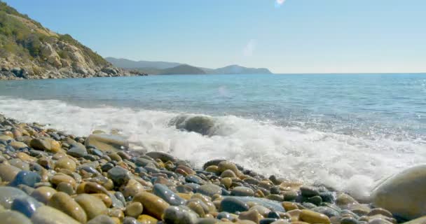 Onde che atterrano su spiaggia di pietra. Acqua cristallina blu . — Video Stock