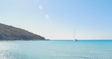 Taş kumsalda açılış dalgalar. Ufukta yat. Açık mavi su.