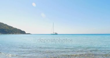 Taş kumsalda açılış dalgalar. Ufukta yat. Açık mavi su.