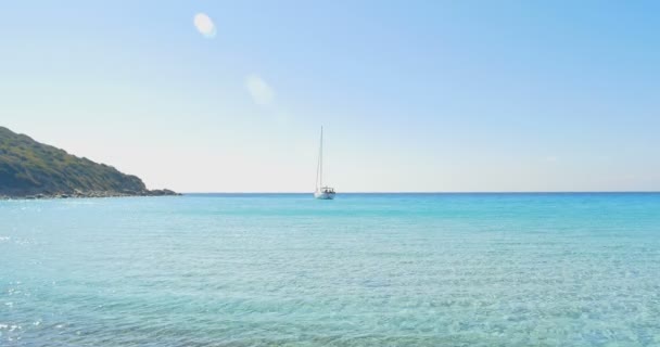 Onde che atterrano su spiaggia di pietra. Yacht all'orizzonte. Acqua cristallina blu . — Video Stock