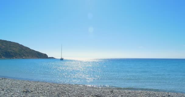 Vagues atterrissant sur la plage de pierre. Yacht à l'horizon. Eau bleue claire . — Video