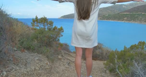 Mladá dívka se zvedl ruce nahoru na kopci nad mořem. Jasné modré mořské vody. — Stock video