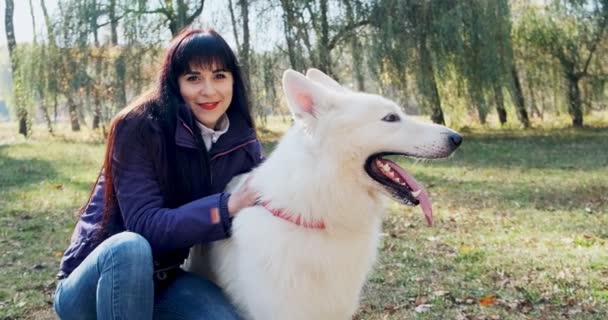 Happy female cheerfully playing and sitting with dog in the autumn park. Love and friendship with domestic animal. White Shepherd — Stock Video