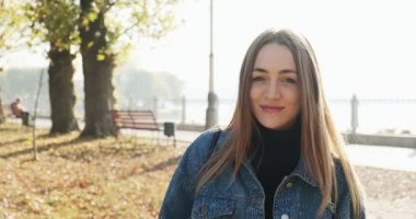 Sonbahar parkında yürüyen mutlu gülümseyen genç kız. Çekici bir kadın güneş ışığında yürür ve gülümser.