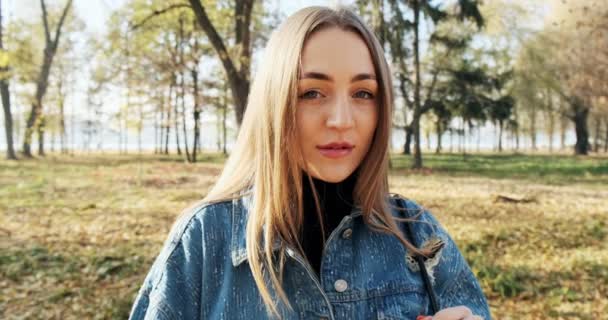 Ritratto di giovane femmina attraente che guarda la macchina fotografica scorrevole su parco di autunno. Allegramente bella donna al tempo soleggiato. Da vicino. — Video Stock
