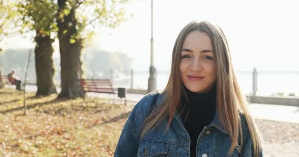 Fiatal boldog mosolygós lány sétál az őszi parkban. Fiatal atraktív nő sétál és mosolyog a napsugarakban — Stock videók