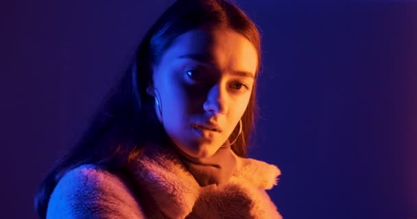 Mooie brunette vrouw poseert in rood en blauw neon licht 's nachts. Fashion model meisje met make-up en cirkel oorbellen in kleurrijke verlichting — Stockvideo