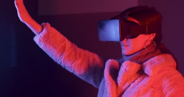 Schöne junge Frau mit Virtual-Reality-Brille auf Neonbeleuchtung Hintergrund. attraktive Mädchen berühren virtuelle Objekte in vr Brille — Stockvideo