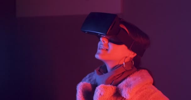 Hermosa mujer joven usando gafas de realidad virtual sobre fondo de iluminación de neón. Chica atractiva tocando objetos virtuales en gafas vr — Vídeo de stock